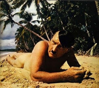 Homme nu, allongé sur une plage, ressemblant à Hitler (moustache, coupe de cheveux)
